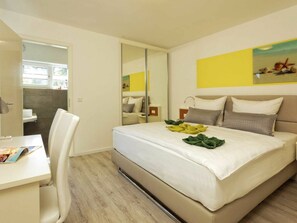 Quarto de hotel com cama, escrivaninha, cadeira, espelho e um quadro na parede.