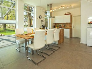 A modern kitchen with a dining area, large windows, and a view of trees. - Holiday Home in Karlshagen With Sauna (Karlshagen)