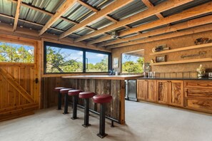 A kitchen with wooden bar stools, a large window, and a rustic ceiling.
