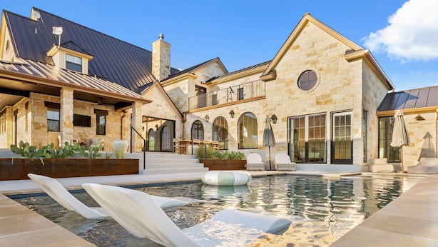 A luxurious house with a swimming pool, stone exterior, and multiple windows. - Deep Eddy Ranch (Dripping Springs)