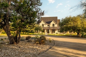 A modern house with a stone facade, a sloped roof, and a driveway leading to the entrance. - Deep Eddy Ranch (Dripping Springs)