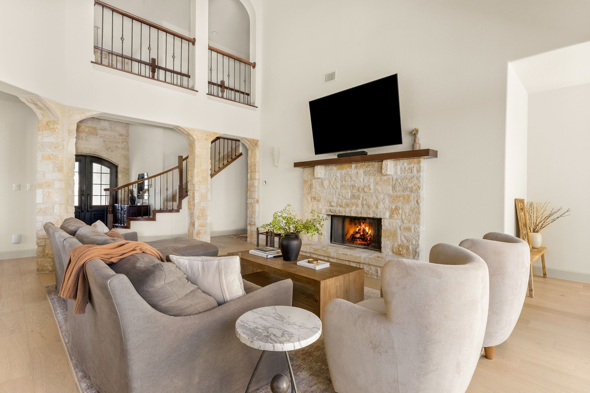A spacious living room with a stone fireplace, a flat-screen TV mounted above it, and a comfortable seating area with sofas and armchairs.