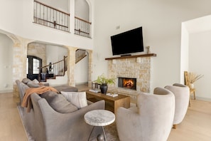 A spacious living room with a stone fireplace, a flat-screen TV mounted above it, and a comfortable seating area with sofas and armchairs.