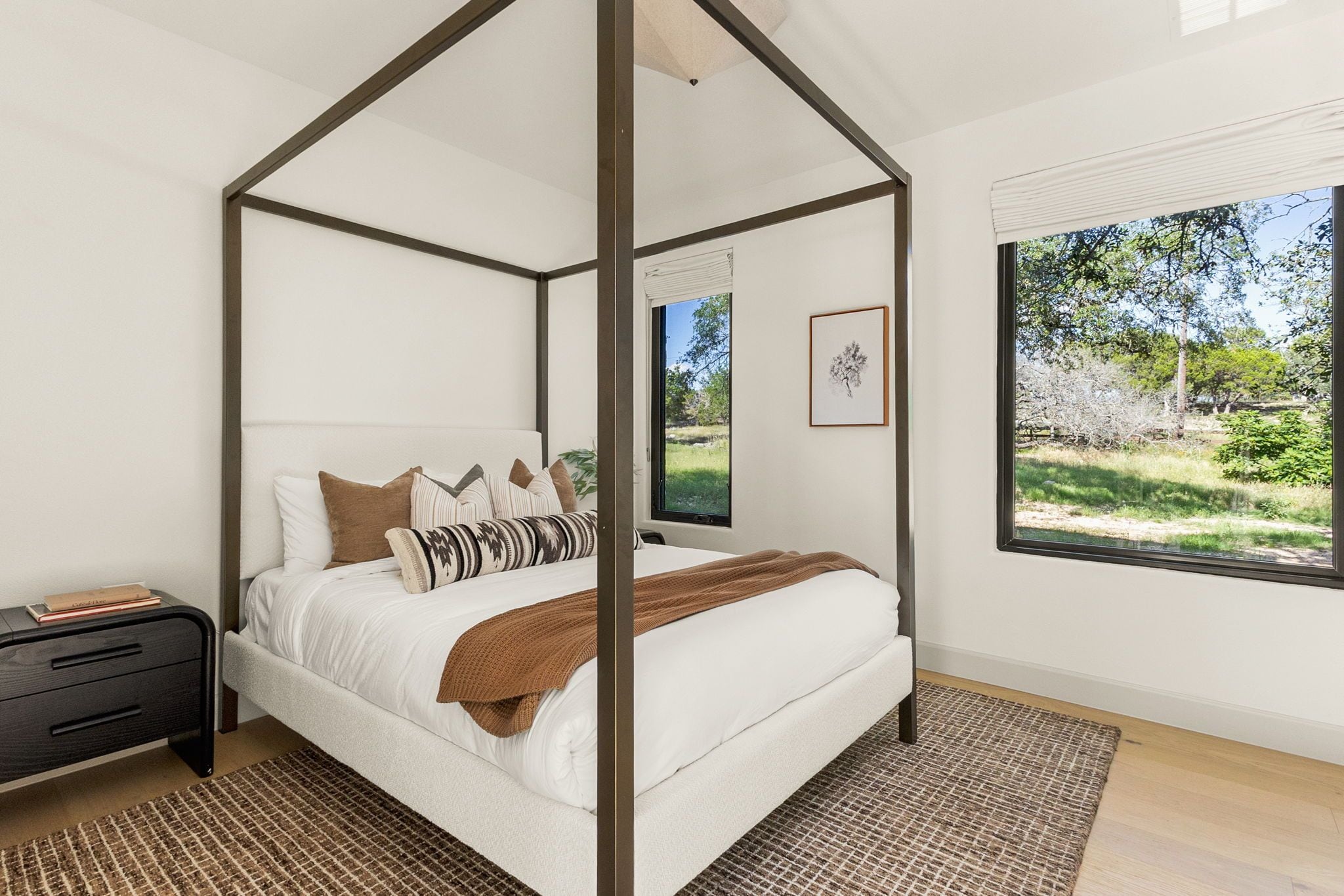 A four-poster bed with a view of a garden through a large window.