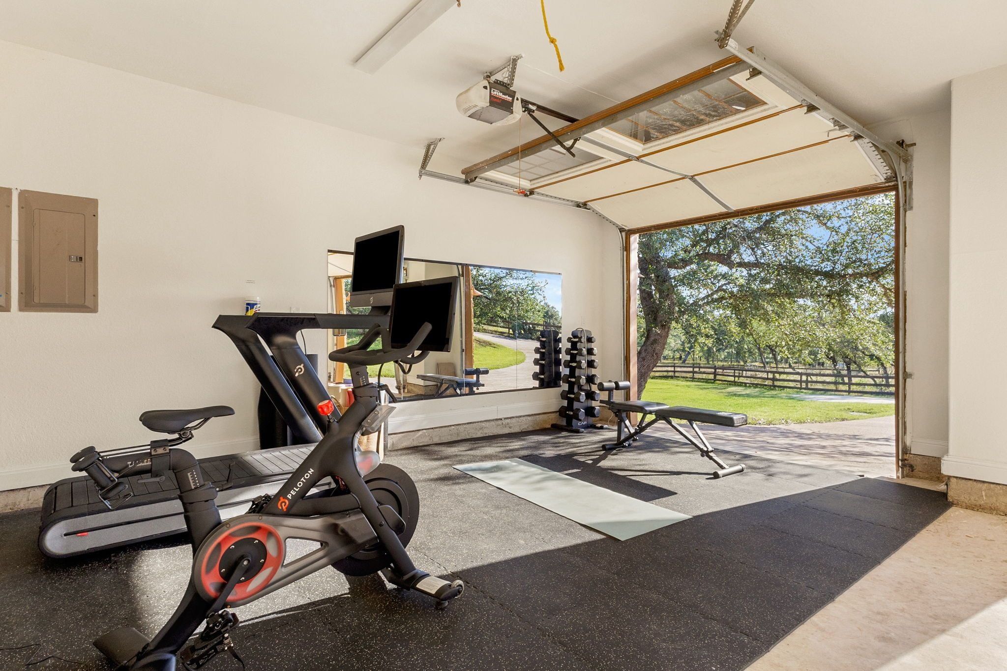 Gimnasio en casa con equipo de ejercicio, televisor y vista a un parque.