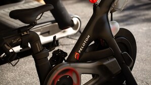 A stationary exercise bike with a red lever and the brand name 'PELOTON' on the frame.