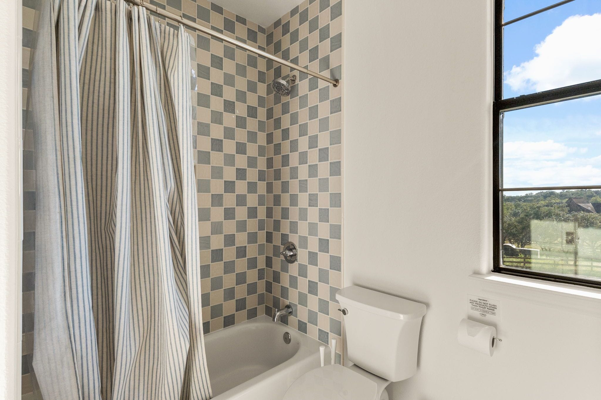 Une salle de bain avec un mur recouvert de carreaux à motifs, une baignoire, des toilettes et une fenêtre donnant sur un paysage agréable.