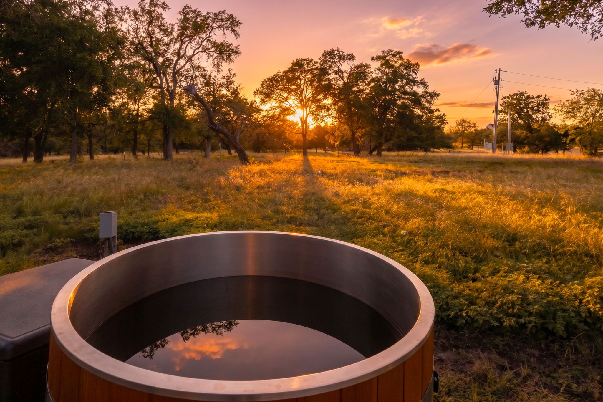 A hot tub in a grassy field with trees and a sunset in the background.