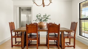 A dining area with a wooden table and chairs, a vase with greenery, and a modern chandelier. - Deep Eddy Ranch (Dripping Springs)