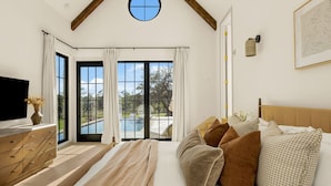 A bedroom with a large bed, a TV, a wooden dresser, and a view of a swimming pool. - Deep Eddy Ranch (Dripping Springs)