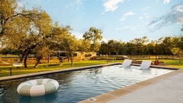 Una piscina con sillas de descanso, un flotador y un área cercada con árboles.