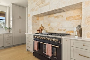A kitchen with a stone wall, a stove, and cabinets. - Deep Eddy Ranch (Dripping Springs)