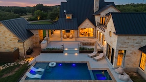 A large house with a swimming pool, outdoor seating, and a well-lit patio area. - Deep Eddy Ranch (Dripping Springs)