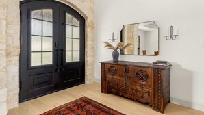 A room with a black double door, a wooden cabinet with carvings, a mirror, and a vase with dried plants.
