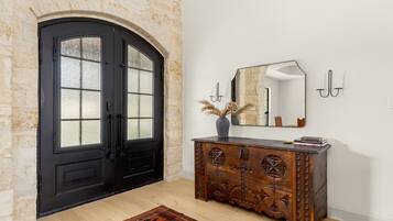 Una habitación con una puerta doble negra, un mueble de madera con adornos tallados, un espejo y un jarrón con plantas secas.