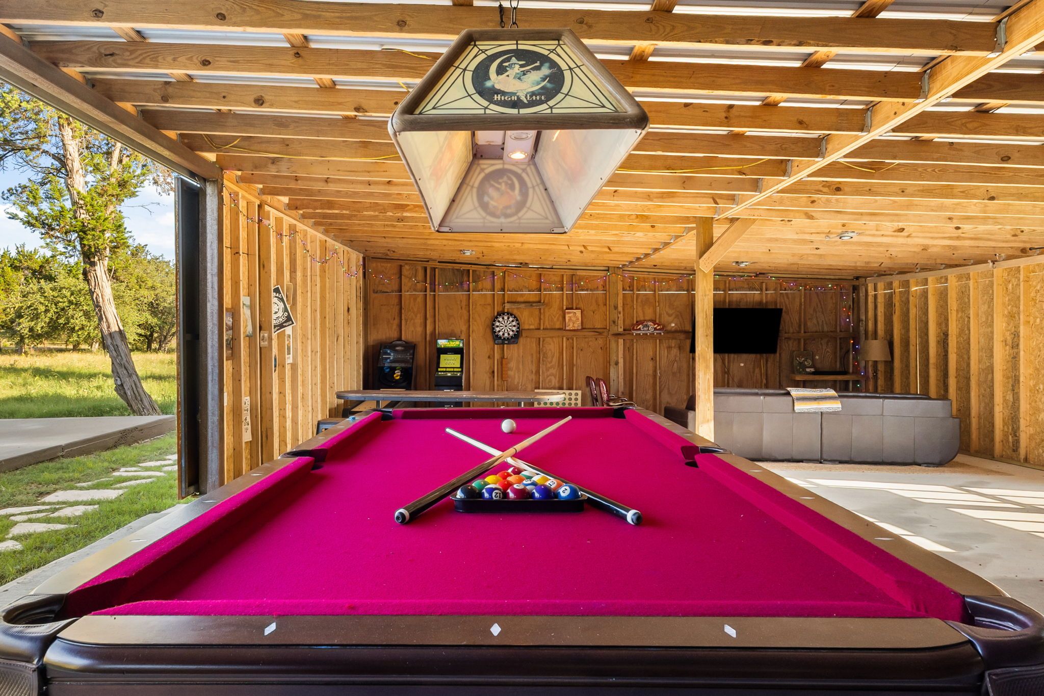 A pool table with a red felt surface, a wooden ceiling with a hanging light fixture, and a billiard cue rack.