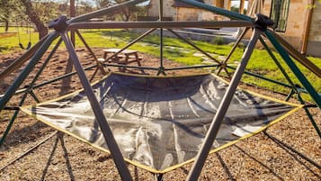 Eine Spielgeräte-Anlage mit einer Kletterwand, umgeben von einer Rasenfläche und einem Steinhaus im Hintergrund.