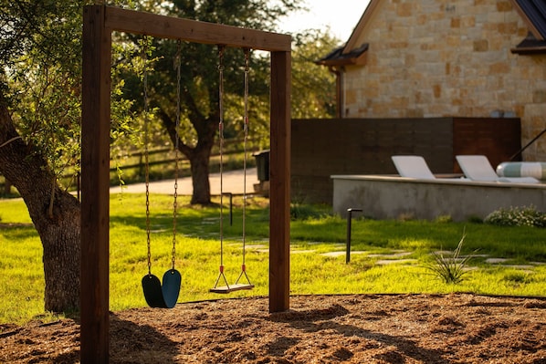 A wooden swing set in a grassy area with a stone building in the background.