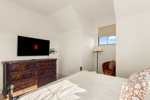 Un dormitorio con cama, cómoda, televisor montado en la pared, lámpara y ventana.