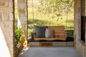 A wooden swing set with cushions, a stone wall, and a grassy area in the background.