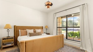 A bedroom with a large bed, two bedside tables, a window with curtains, and a hanging light fixture.