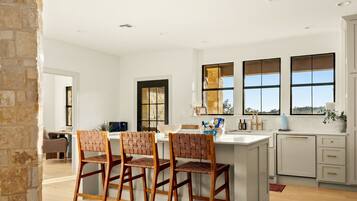 A modern kitchen with a central island, bar stools, and a view of the outdoors through large windows.
