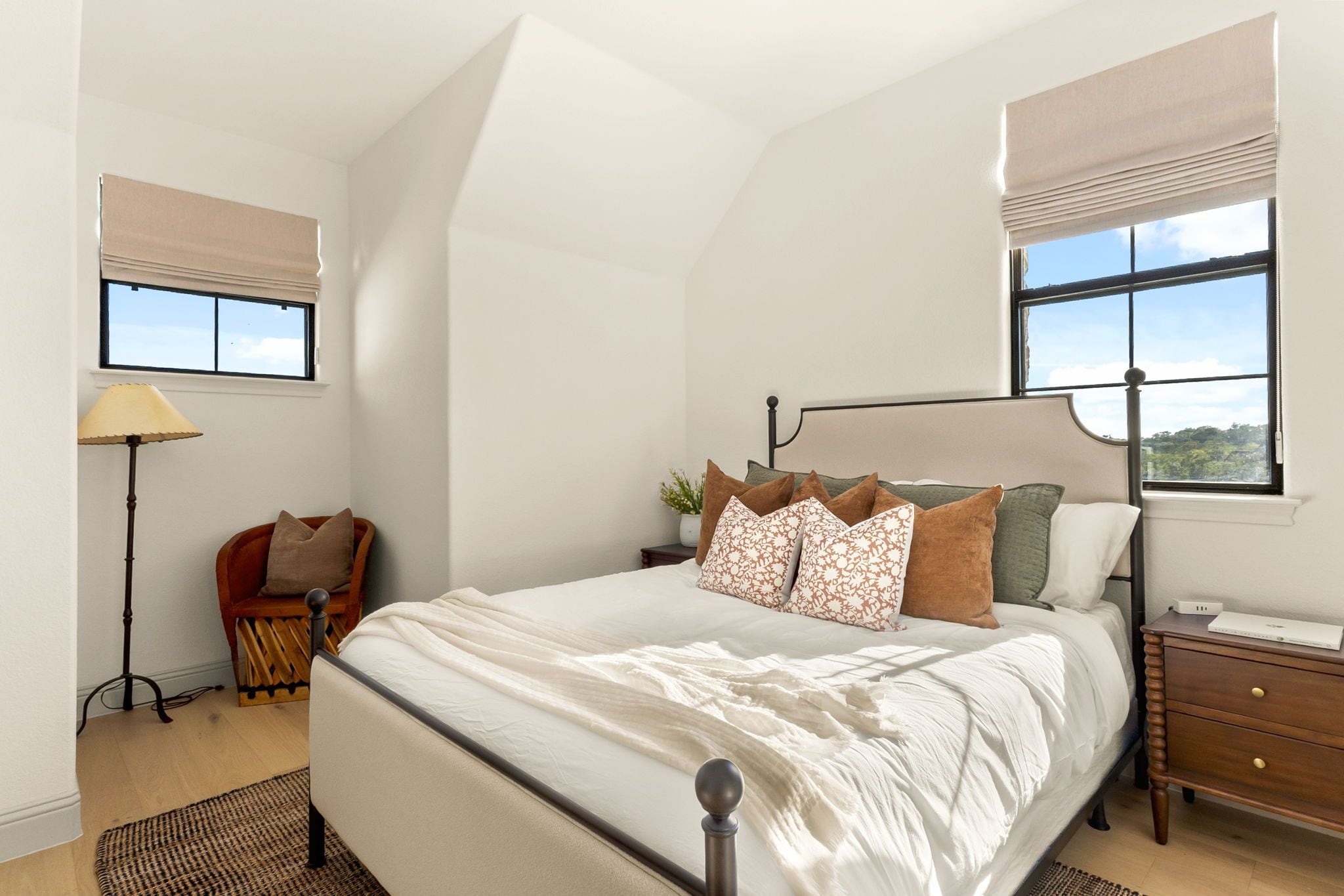 Un dormitorio con una cama grande, una mesita de noche, una lámpara, una silla y dos ventanas con persianas.