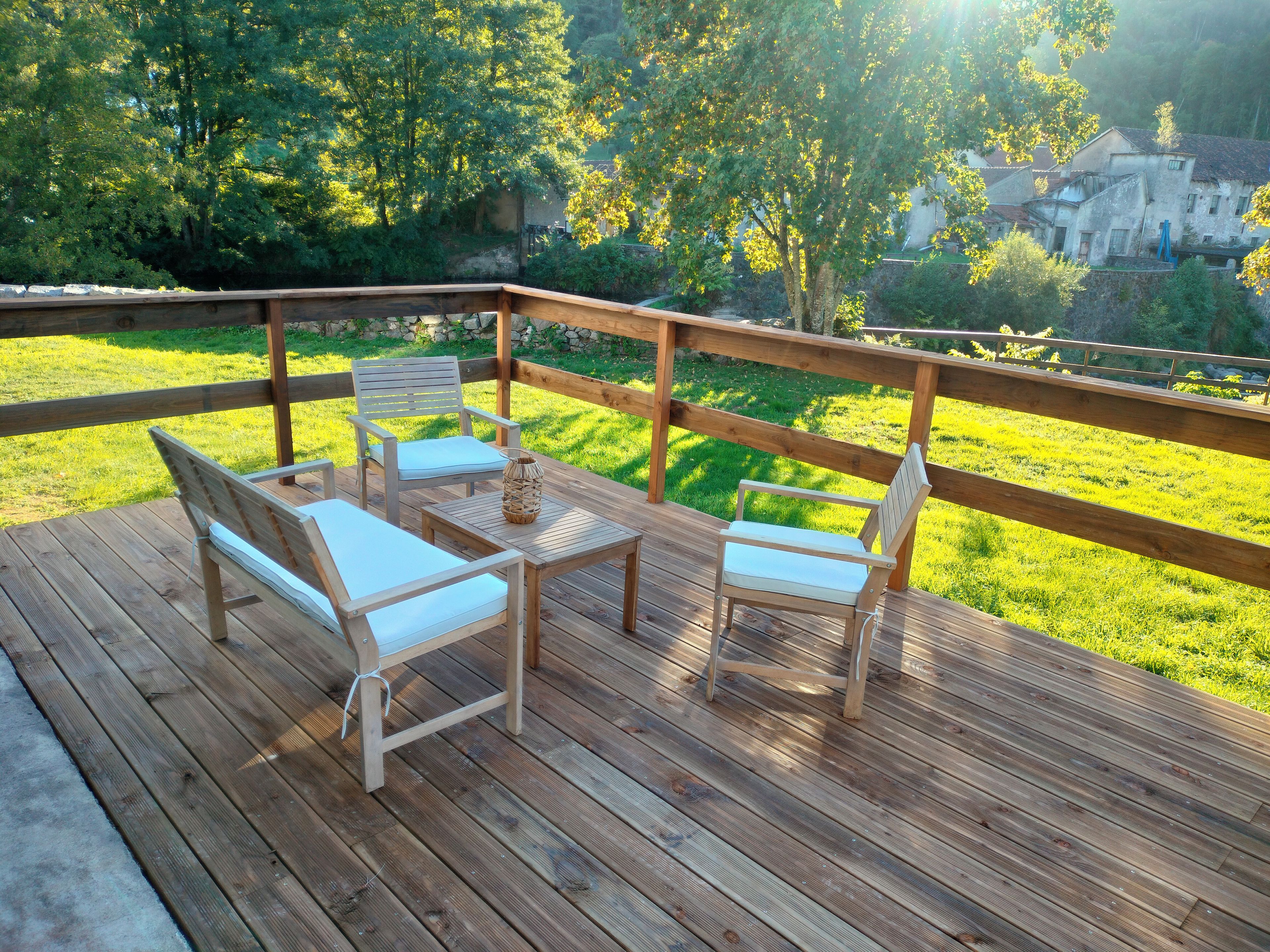 Een houten terras met een tafel en stoelen, met uitzicht op een gazon en een gebouw op de achtergrond.