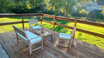 Een houten terras met een tafel en stoelen, met uitzicht op een gazon en een gebouw op de achtergrond.