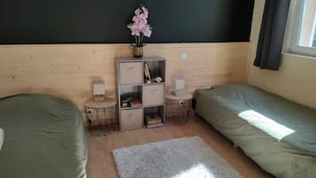 Een slaapkamer met twee bedden, een klein tafeltje met een lamp, een boekenkast en een raam met gordijnen.
