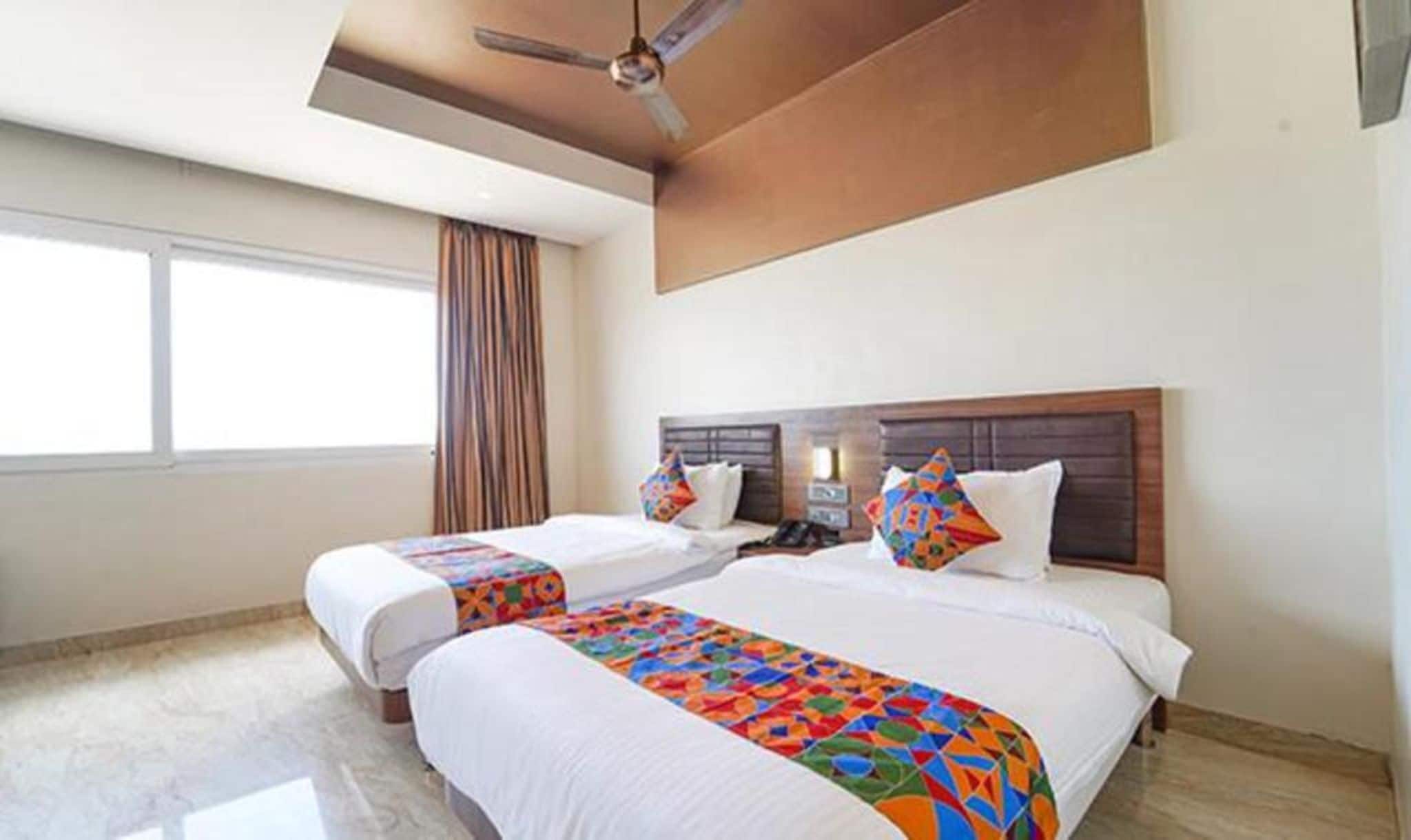A hotel room with two beds, a ceiling fan, a window with curtains, and a tiled floor.