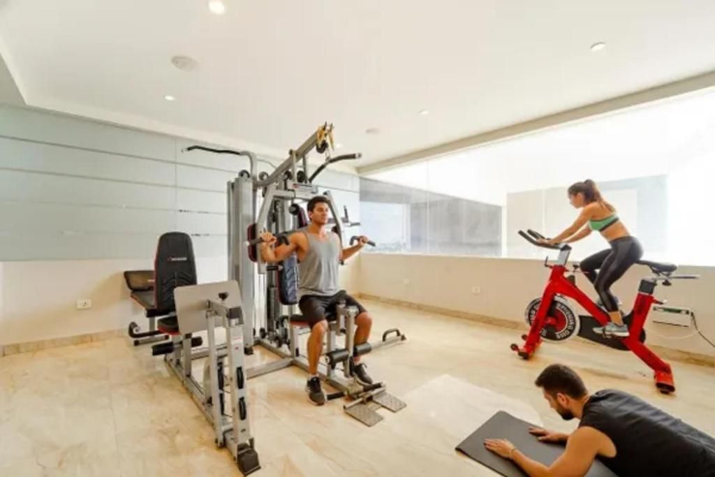 Academia com equipamentos de ginástica, uma bicicleta ergométrica e uma pessoa se exercitando em um tapete.