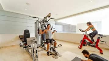 Academia com equipamentos de ginástica, uma bicicleta ergométrica e uma pessoa se exercitando em um tapete.