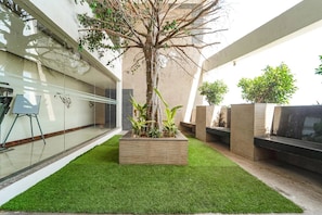 Zona exterior moderna amb gespa artificial, un arbre i jardineres.