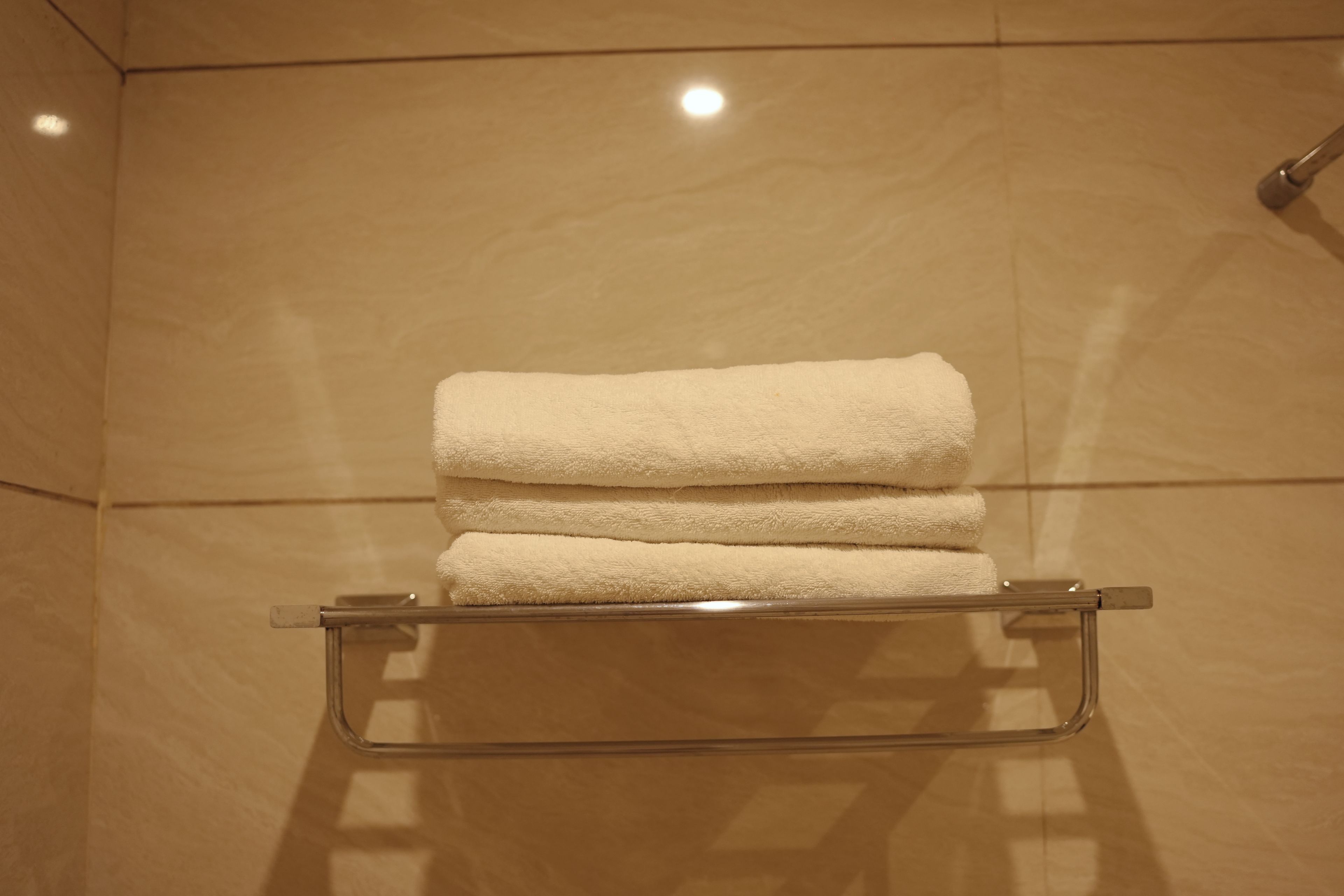 Un baño con repisa de vidrio que sostiene tres toallas dobladas.