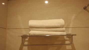Un baño con repisa de vidrio que sostiene tres toallas dobladas.