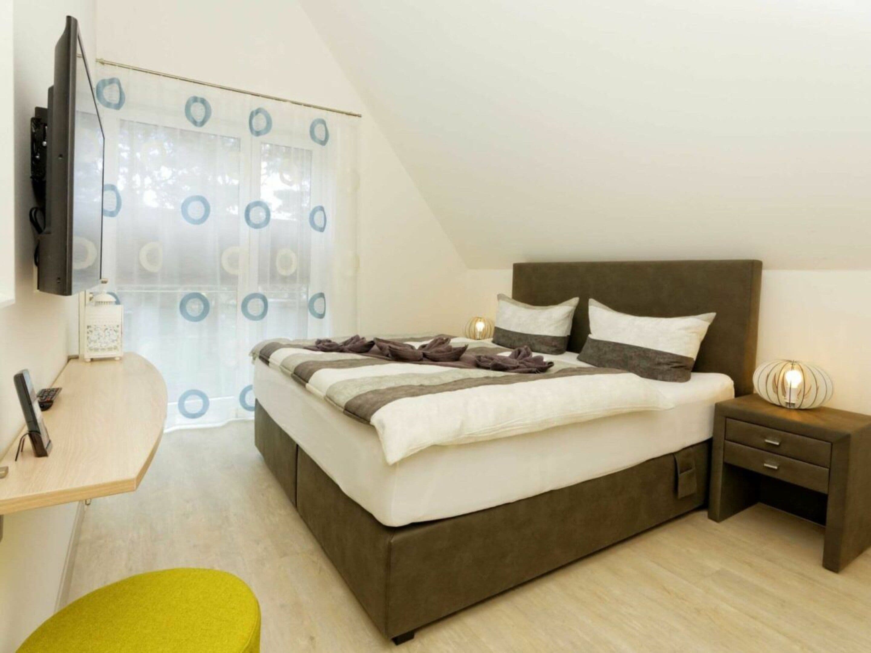 A hotel room with a bed, bedside table, lamp, and a TV mounted on the wall.