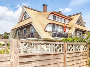 A two-story house with a steeply pitched roof, a balcony with a railing, and a wooden fence in the foreground. - Holiday Apartment With 1 Bedroom (Zingst)