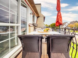 A balcony with wicker furniture, a table with a tray of food, and a red umbrella. - Holiday Apartment With 1 Bedroom (Zingst)