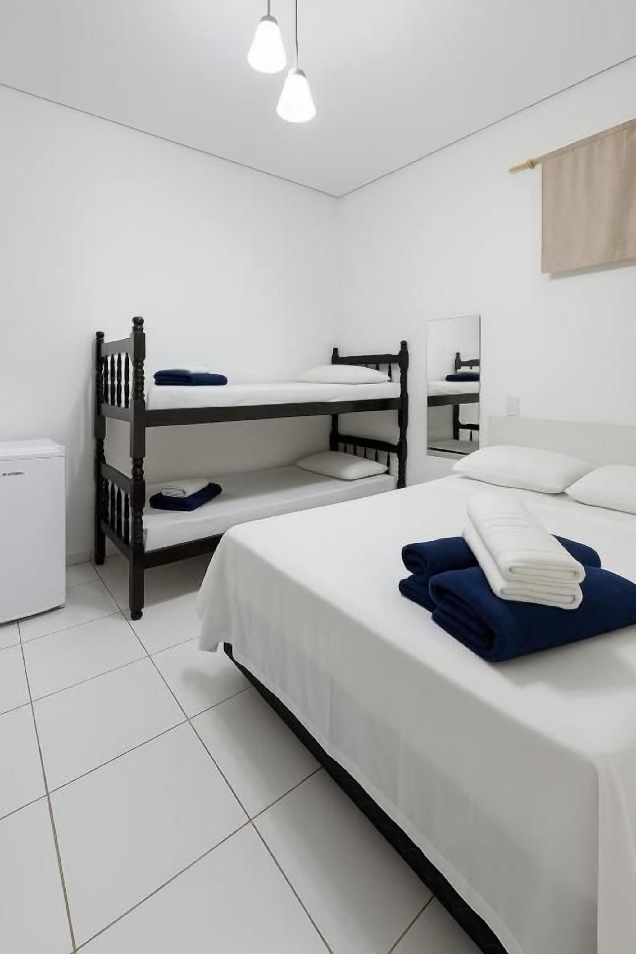 A room with bunk beds, a small desk, a mirror, and a white tiled floor.