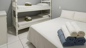 Een kamer met een stapelbed, een enkel bed, een nachtkastje en een opgerolde handdoek op het bed.