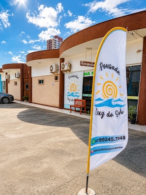 A building with a reception area, a flag with a sun and waves design, and a contact number. - Pousada Luz do Sol  (Penha)