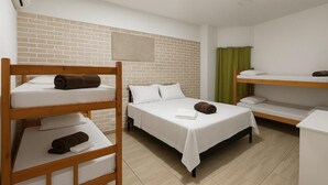 Habitación de hotel con literas, una pared de acento de ladrillo, una cortina verde y una mesita de noche blanca.