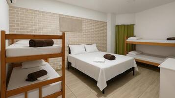 A hotel room with bunk beds, a brick accent wall, a green curtain, and a white bedside table.