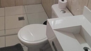 Een kleine badkamer met tegels, een toilet, een wastafel en een douchecabine.