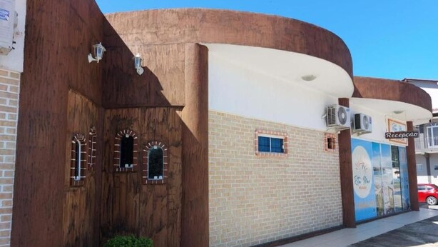 Un edificio con fachada de ladrillo, estructura de madera a la izquierda y un cartel con la palabra 'Recepcao' a la derecha.