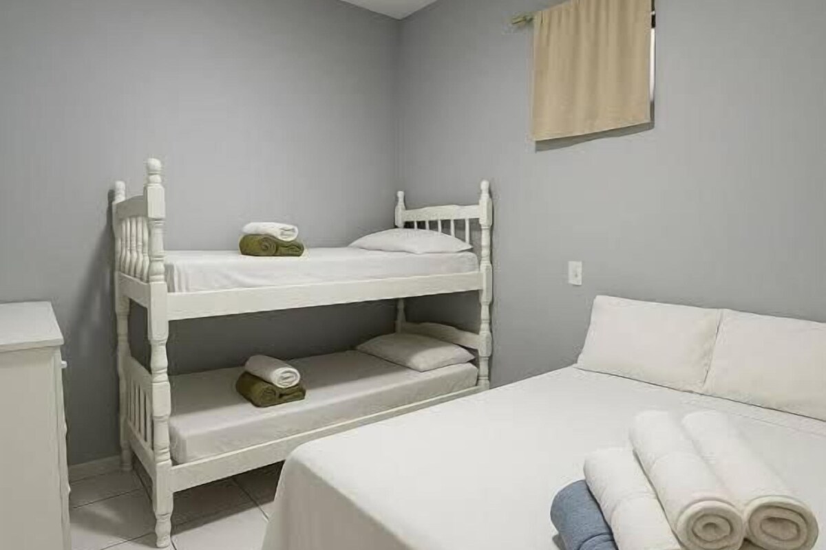 Una habitación con literas, una cama individual, una mesita de noche y una toalla enrollada sobre la cama.