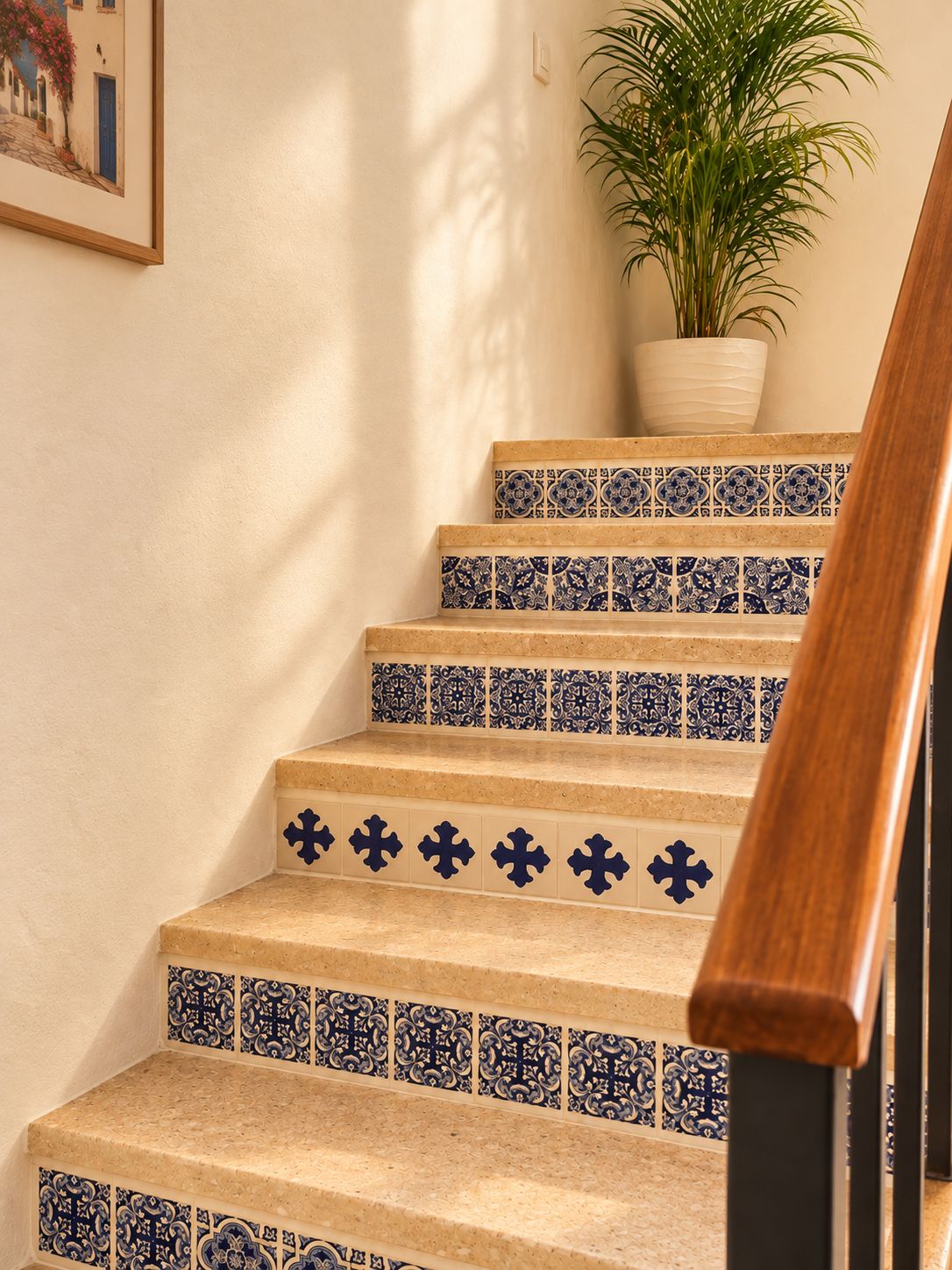 Una escalera con baldosas de diseño azul y blanco, barandilla de madera y una planta en el descansillo.