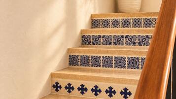Una escalera con baldosas de diseño azul y blanco, barandilla de madera y una planta en el descansillo.