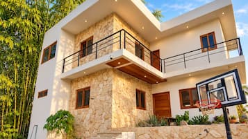 A modern two-story house with a stone facade, a balcony, and a basketball hoop.